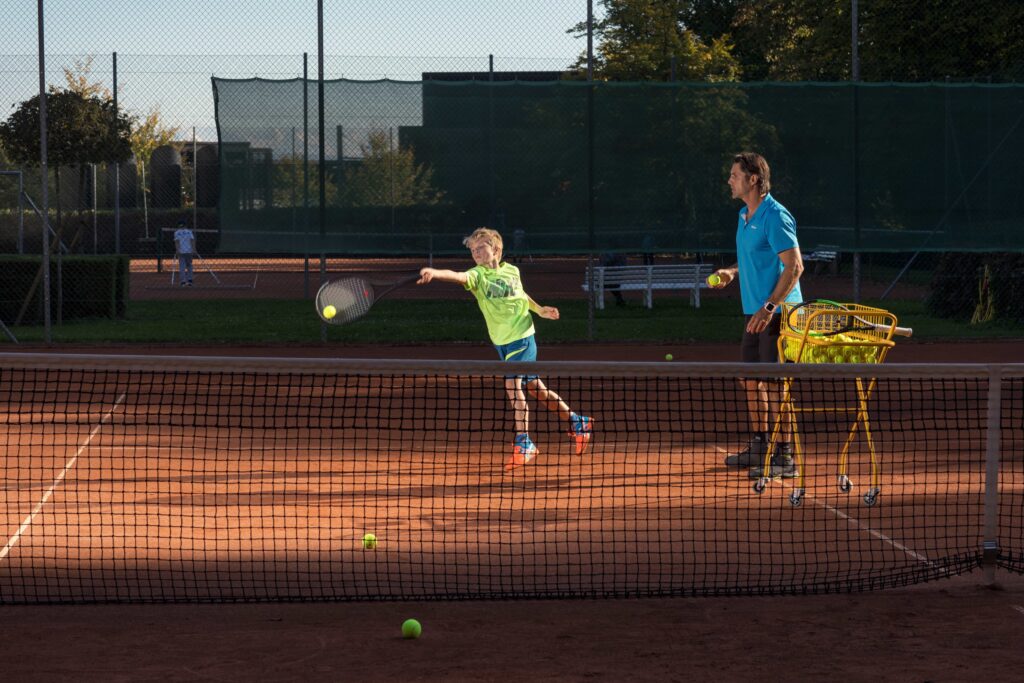 Kind beim Tennistraining mit Trainer Sven Melig, Fokus auf Schlagtechnik und Präzision am Netz, Kids Sportcamps.
