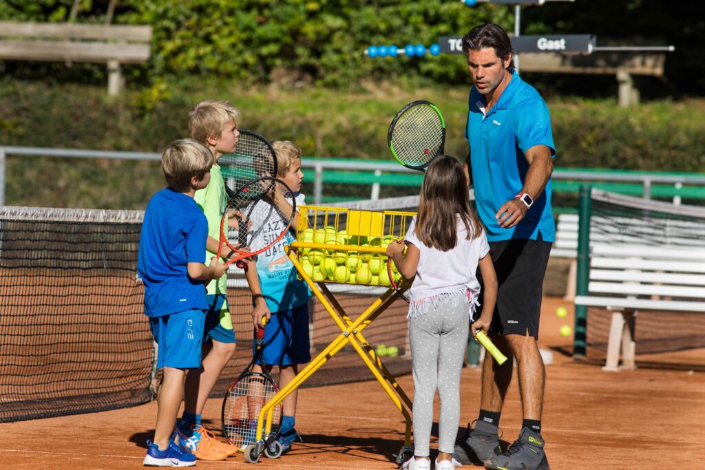 Trainer Sven Melig erklärt Kids Sportcamps-Teilnehmer:innen am Tennisballkorb die nächste Trainingsrunde, Tennisclub Weihermatt.